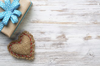 Flat lay cute composition with handmade fabric heart. Gift box with ribbon bow on wooden table.