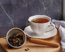 White ceramic tea cup and strainer with tea leaves on wooden board on windowsill, copy space