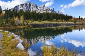 Bright autumn forest is reflected in the smooth water of the lake. The city of Canmore. Three