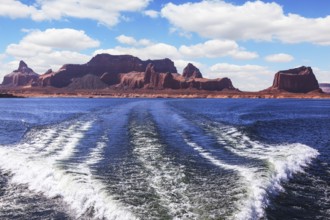 Foamy trace of a motor boat crosses the emerald waters. In distance the coast of red sandstone.