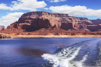 Foamy trace of motorboat crosses the emerald waters. Red sandstone hills surround the lake. Lake