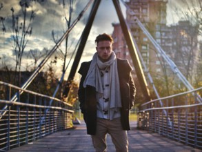 Handsome young man in city setting, with industrial site around him, looking at camera, serious