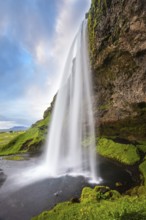 Sunny day in Iceland. Seljalandsfoss waterfall in July. Passage under the waterfall