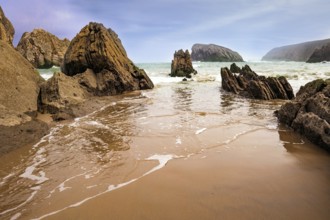 The smooth wet sand of the beach reflects the rocky boulders. The Playa de la Arnia beach.