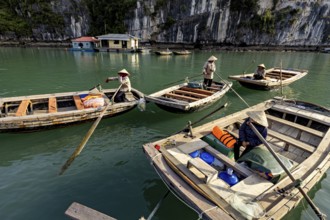 Boats with people in front of a rock, during a calm river trip, rowing boats for tourists in Halong