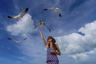 A stunning woman gracefully feeds seagulls on a Caribbean beach, surrounded by turquoise waters and