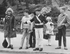 Junior safety patrol in the 1960s. A teenage boy stands with his arms out and signals to the