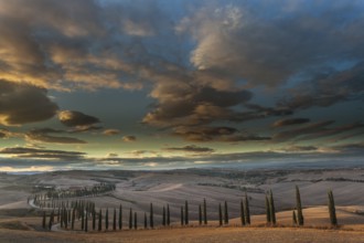 Tuscan hilly landscape with cypresses under a dramatic sky, Asciano, Province of Siena, Tuscany,