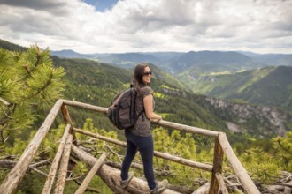 Young tourist woman with backpack enjoys the view from a wooden bridge high in the mountain