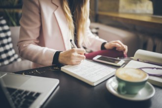 Close up caucasian woman hand on wooden table inside cafe makes notes in notebook. Subject