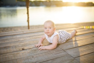 A child a boy, one year old, blond man lies on his stomach on wooden dock, pier in striped clothes,