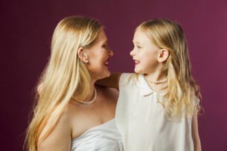 Portrait of happy smiling mother and daughter, both with long loose blond hair, wearing white