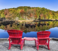 Red plastic loungers on the shore of the pond. Foliage of forests is reflected in the pond.