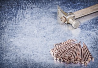 Vintage claw hammer stack of copper construction nails on metallic background