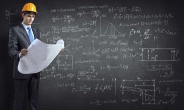 Young thoughtful man engineer in helmet with project in hands and sketches on wall
