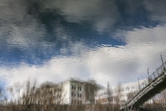 Building and part of a bridge are reflected in the river Mur, Leoben, Styria, Austria, Europe