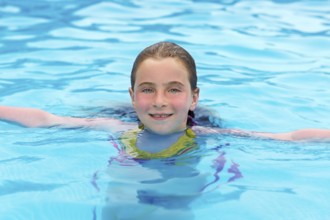 Blond kid girl swimming in the pool with sun tan red cheeks