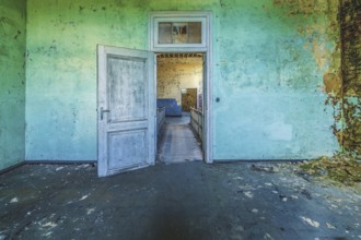 Open wooden door in a dilapidated room with peeling green wall paint, Prison H11, Lost Place,