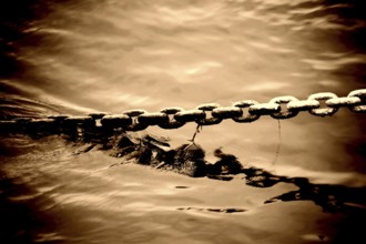 The bizarre and brute toning of an anchor chain protruding from a body of water