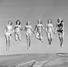 1940s summer. A group of young women in their bikinis are happy on this summer's day, jumping of