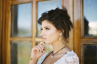 Woman touches her chin with her fingers against the backdrop of a glass door. Close-up.