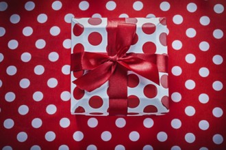 White present box with tied ribbon on polka-dot red fabric celebrations concept