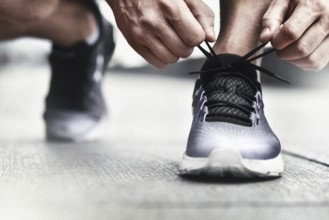Cropped image of hands tying shoelaces on sneaker, running surface background. Hands of sportsman