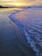 A serene beach scene with gentle waves reflecting a vivid sunset sky, creating a calm and peaceful