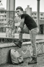 Attractive young man wearing black T-shirt and jeans with back pack standing outside