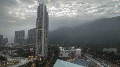 Cloudy sky over Hong Kong. Evening cityscape with high-rise buildings and green mountain