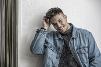Handsome white asian young man wearing blue denim jacket, standing on light background against wall