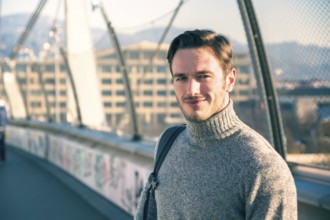 Handsome young man walking in city with backpack on one shoulder, wearing winter clothes