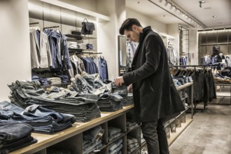 Side view of young male customer choosing shirt in menswear shop