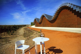 Table and chairs for tourists. Fragment of the facade. Wave-shaped winery roof. Winery - bodega