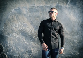 One handsome young man in urban setting in European city, standing, wearing black jacket and jeans