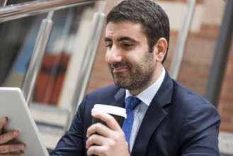 Confident businessman sitting on steps with tablet and coffee