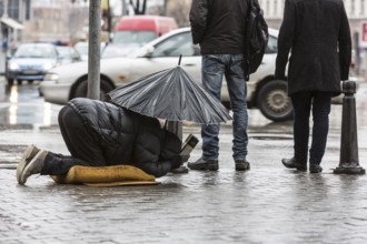 Homeless beggar is begging for money in a main street in Sofia holding an umbrella in a rainy day.