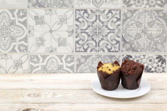 Two tempting muffins on a white plate against a vintage tile backdrop create an inviting scene to