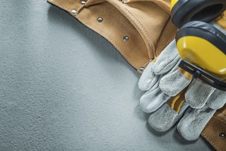Set of leather tool belt safety gloves earmuffs on concrete background
