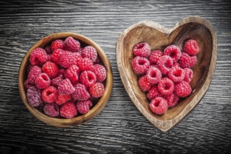 Round and heart-shaped bowls with raspberries on wooden board