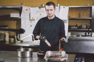 Theme cooking. A young Caucasian man in black uniform and latex gloves at a restaurant in the