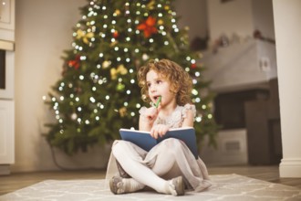 Sweet dreamy little girl with curly hair, wearing grey dress, sitting in front of decorated