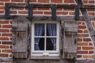 Rustic window with wooden frame and blue chequered curtains in a half-timbered house, weseke,