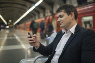 Young businessman using smartphone while waiting at the underground station. Blurred platform,