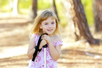 Beautiful kid girl in park forest smiling with trekking pole