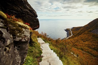 A stone path leads to a scenic view of the sea and a winding road down the hill, mountains, rocks,