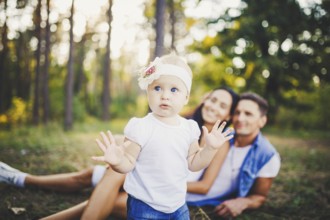 Little girl one year on the background of parents resting on graß learning to walk on nature in the