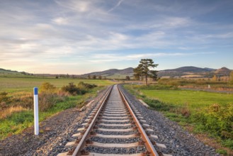 Old Railway tracks running through a field stretch to rural countryside at sunset. Single railway