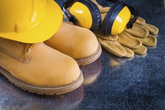 Waterproof boots leather protective gloves earmuffs and building helmet on scratched metallic