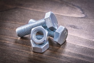 Couple of steel bolt details and screw nuts on vintage brown wooden board construction concept